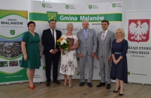 grupa osob pozuje na tle scianki z napisem gmina malanow (2)