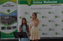dwie dziewczyny spiewaja do mikrofonu w tle scianka z napisem gmina malanow